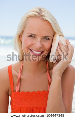 Woman holding a shell to hear the sound of the sea while showing a great smile
