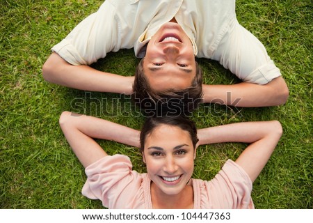 Man and a woman smiling while lying head to head with both of their arms resting behind their neck on the grass