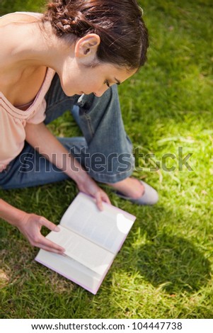 Woman looks down while reading a book as she sits on the grass on a sunny day