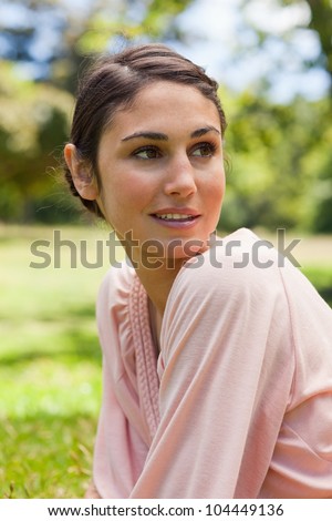 Woman with curious expression on her face looking towards the side as she sits down on the grass