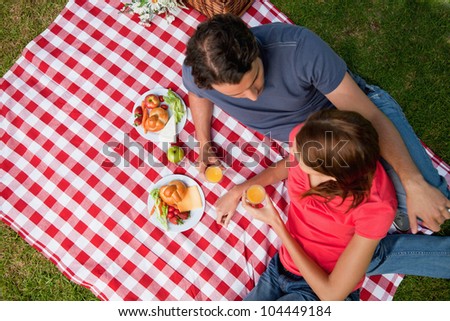 Elevated view of two friends looking into each others eyes while they hold glasses as they lie on a blanket with a picnic