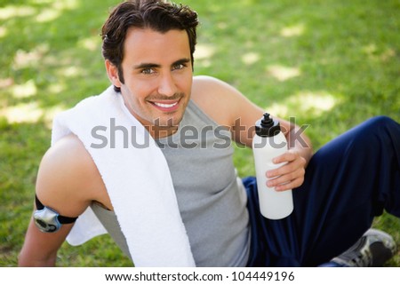 Man smiling with a white towel on his shoulder looking at the camera while holding a sports bottle