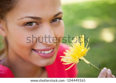 Woman looking towards the camera while holding a yellow flower with grass in the background