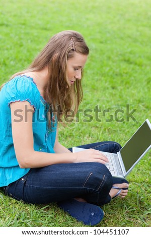 Young serious girl sitting cross-legged in the countryside while typing on her laptop