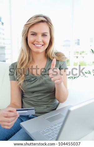 A woman with credit card in hand and laptop beside her, smiles giving a thumbs up.