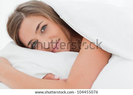 A close up shot of a woman lying in bed with her head on the pillow as she looks forward.
