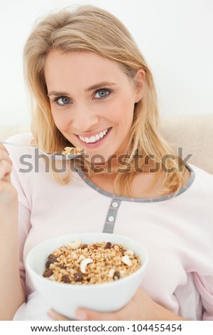 A close up shot of a woman with a raised spoon of cereal by her mouth as she smiles and looks ahead.
