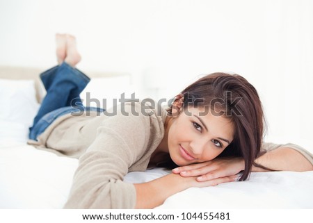 A woman lies, with her feet crossed, on the bed and with her hands under her head.