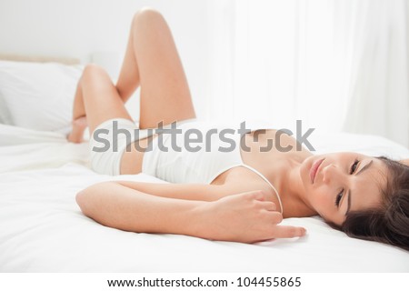 A woman is lying on her back as she glances to the side, while her arm is beside her head and her knee is slightly raised.