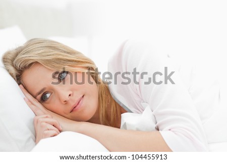 A woman in bed with her hands on the pillow just beside her head and her eyes open glancing to just in front of her.