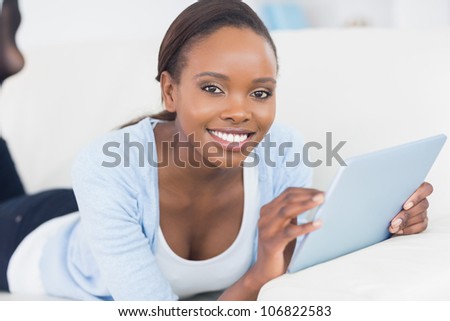 Black woman smiling while holding a tablet computer in a living room