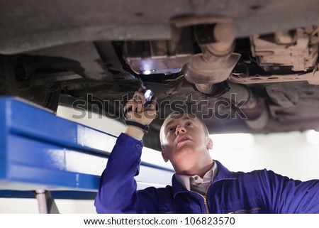 Mechanic looking at a car while holding a flashlight in a garage