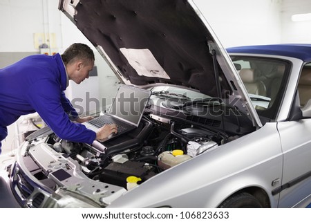 Mechanic typing on a computer while looking it in a garage