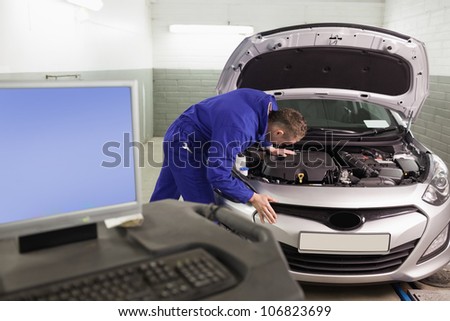 Mechanic repairing a car next to a computer in a garage