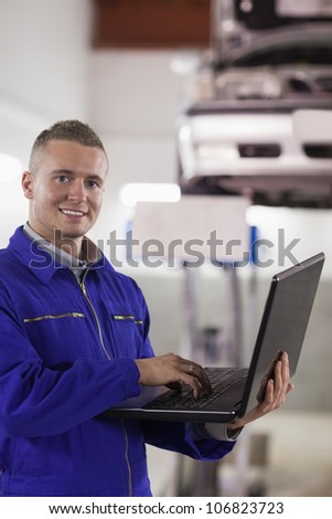 Smiling mechanic typing on a laptop in a garage