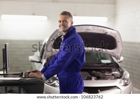 Smiling mechanic typing on a computer in a garage