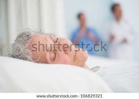 Elderly patient sleeping on a bed next to a doctor in hospital ward