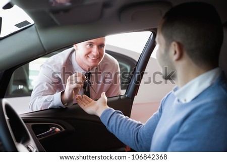 Smiling salesman giving keys to a customer in a car