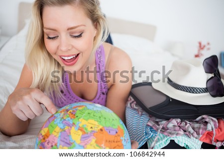 Woman with a suitcase pointing on a globe while lying on her bed