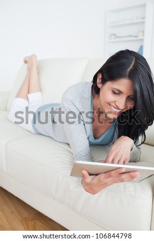 Smiling woman lying on a couch and plays with a tactile tablet in a living room