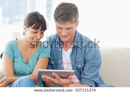 A smiling couple sitting together as they use a tablet pc