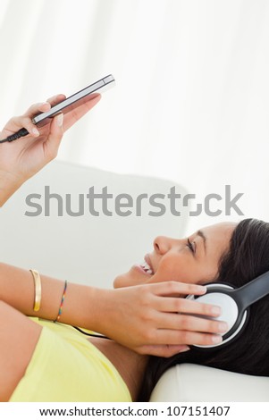 Close-up of a young Latino watching a video with earphones on her smartphone while lying on a sofa