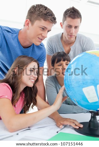 A close up shot of four people sitting in front of the globe and looking for a place