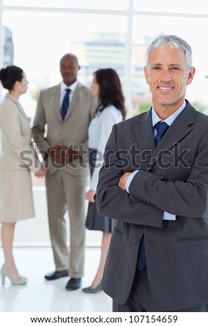 Mature smiling manager crossing his arms in front of his business team
