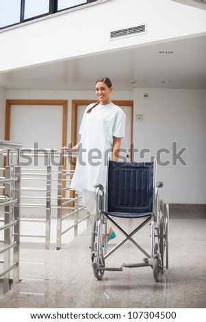 Smiling patient standing next to a wheelchair in hospital hallway