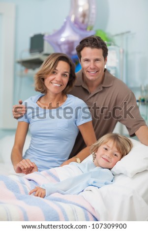 Child lying on a medical bed next to his parents in hospital ward