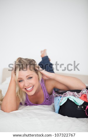 Laughing woman lying next to her full suitcase on her bed