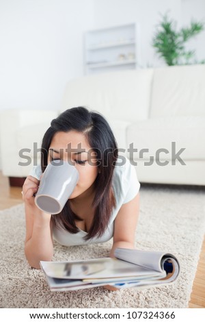Woman drinking from a mug while holding a magazine in a living room