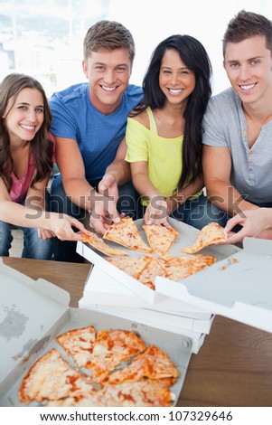 A smiling group of friends as they look into the camera and take some pizza