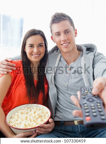 A close up shot with focus on the couple sitting on the couch with popcorn as they use a remote to change the tv
