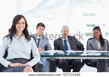 Young executive sitting with her hand on her leg and accompanied by her team in the background