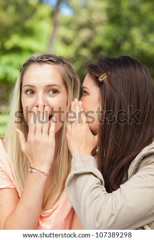 Close-up of female teenagers sharing a secret with hands in front of the mouth in a park