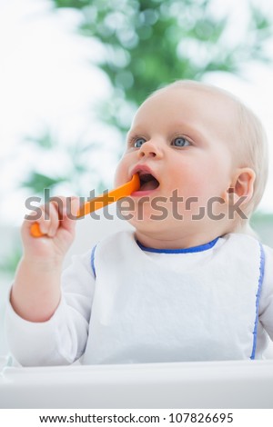 Baby holding a plastic spoon while putting it in his mouth in living room