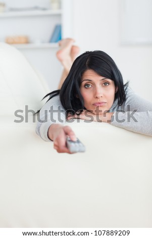 Woman pressing on a television remote while laying on a sofa in a living room