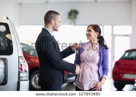 Woman shaking the hand of a salesman while receiving car keys in a car shop