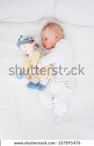 Baby sleeping while embracing a plush doll in a bedroom