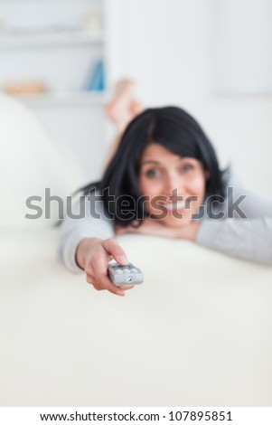 Woman pressing on a remote control while laying on a sofa in a living room