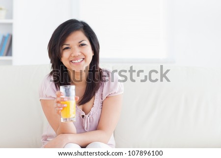 Woman smiling and sitting in a couch while holding a glass of orange juice in a living room