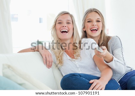 Laughing sisters on the couch as they watch tv and look at the camera