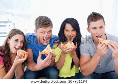 A smiling group with mouths open about to eat pizza as they look at the camera