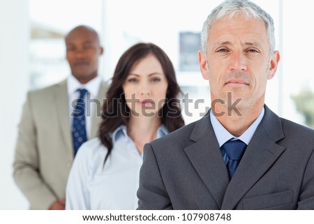 Mature manager standing upright and followed by two serious employees
