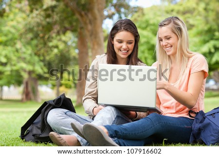 Laughing teenagers sitting while using a laptop in a park
