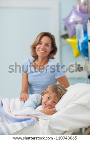 Child lying on a bed next to his mother in hospital ward