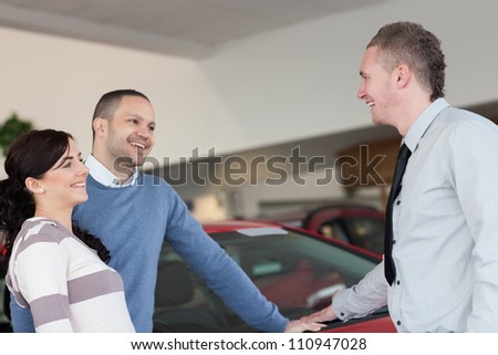 Laughing couple talking with a salesman in a car shop