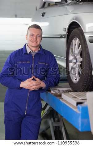 Front view of a smiling mechanic next to a car in a garage
