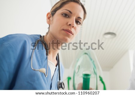 Nurse holding an oxygen mask while looking at camera in hospital hallway